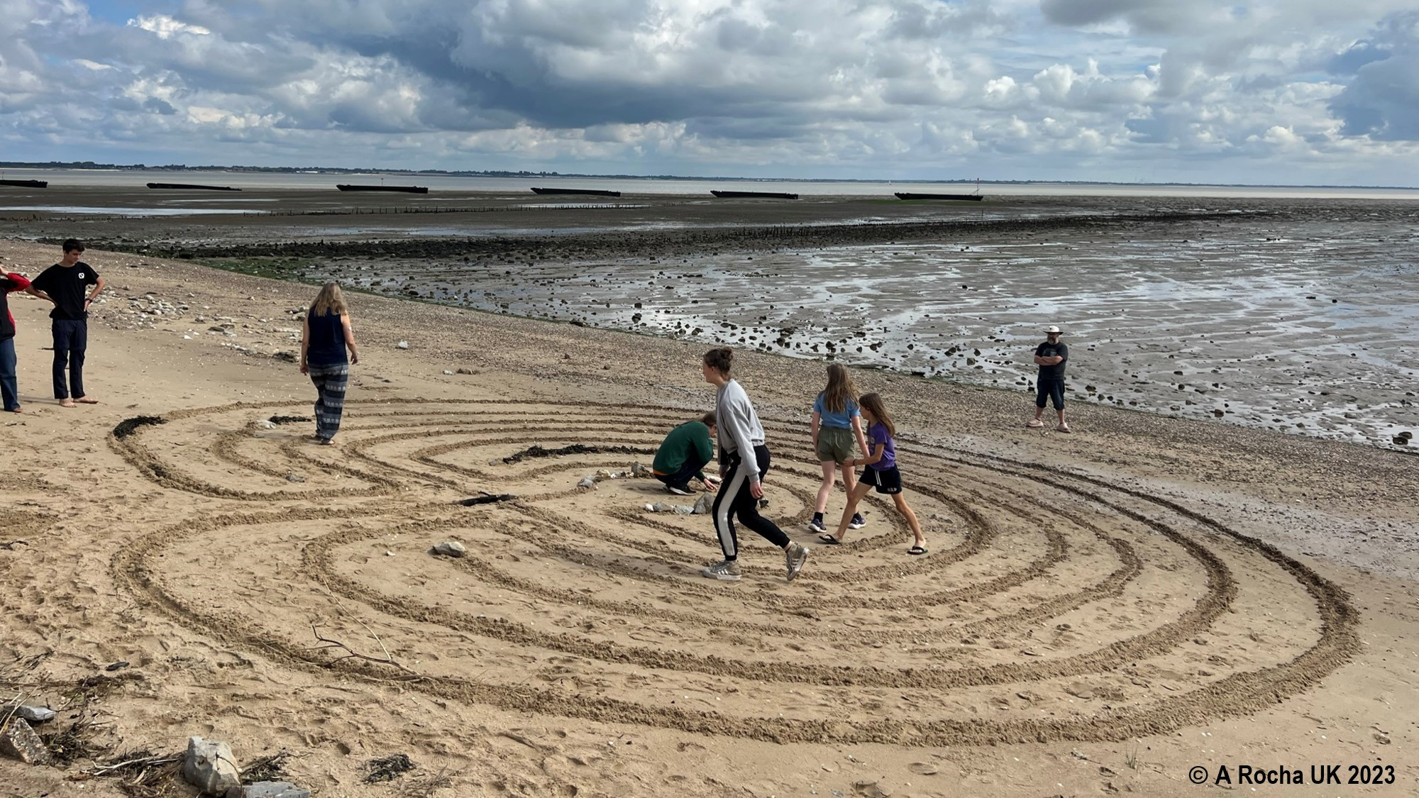 People walking round a sandy beach labyrinth