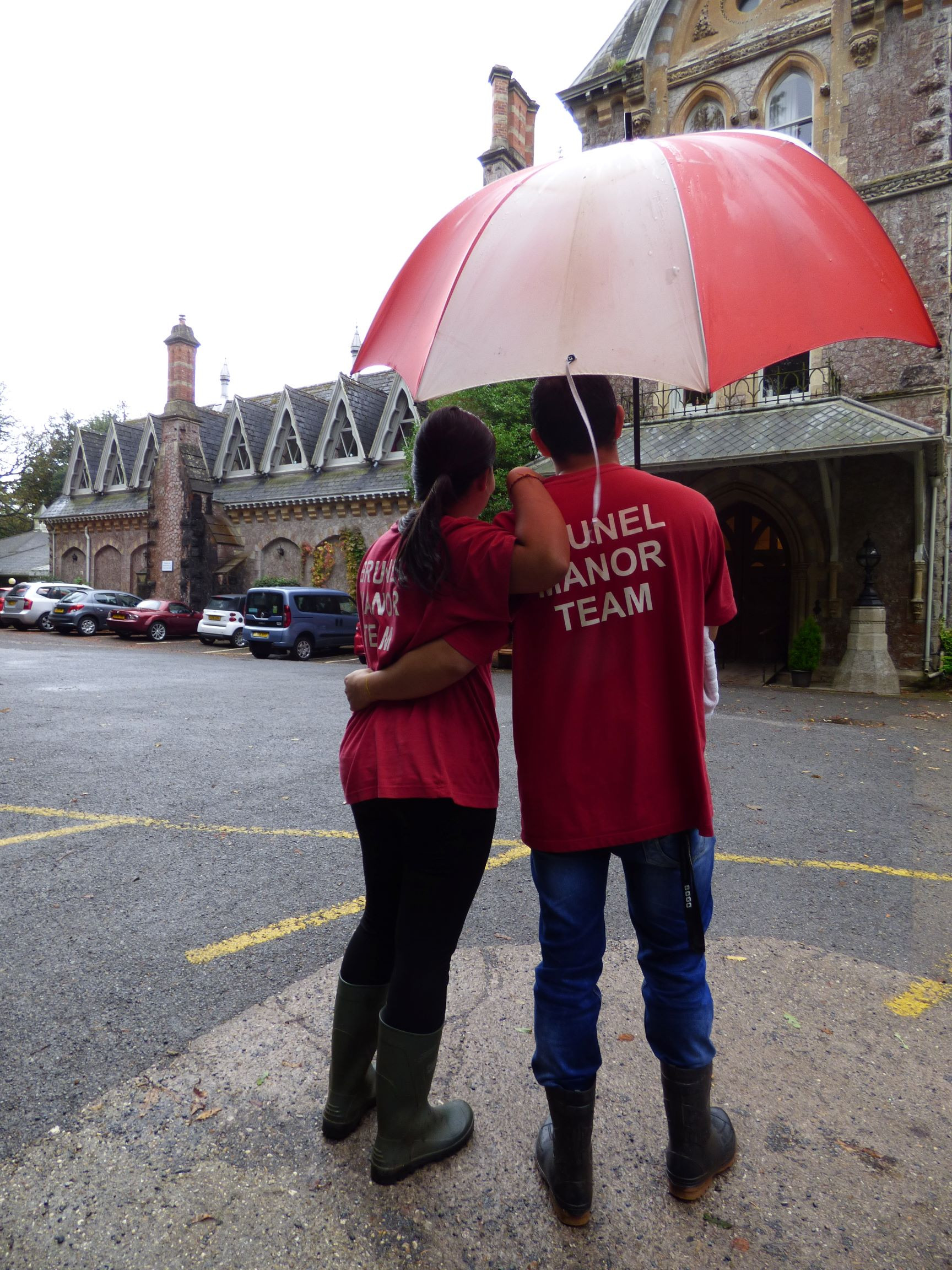 2 Brunel Manor team members standing under an umbrella in the rain